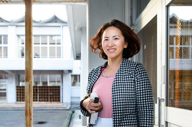 開発した商品を持って元小学校の建物に立つ杉岡雪子さん。