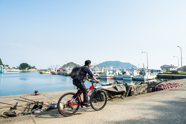 漁港の近くを自転車で走る今村シェフ