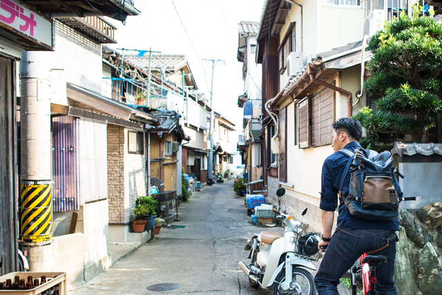 漁村の路地を自転車で走る今村シェフ